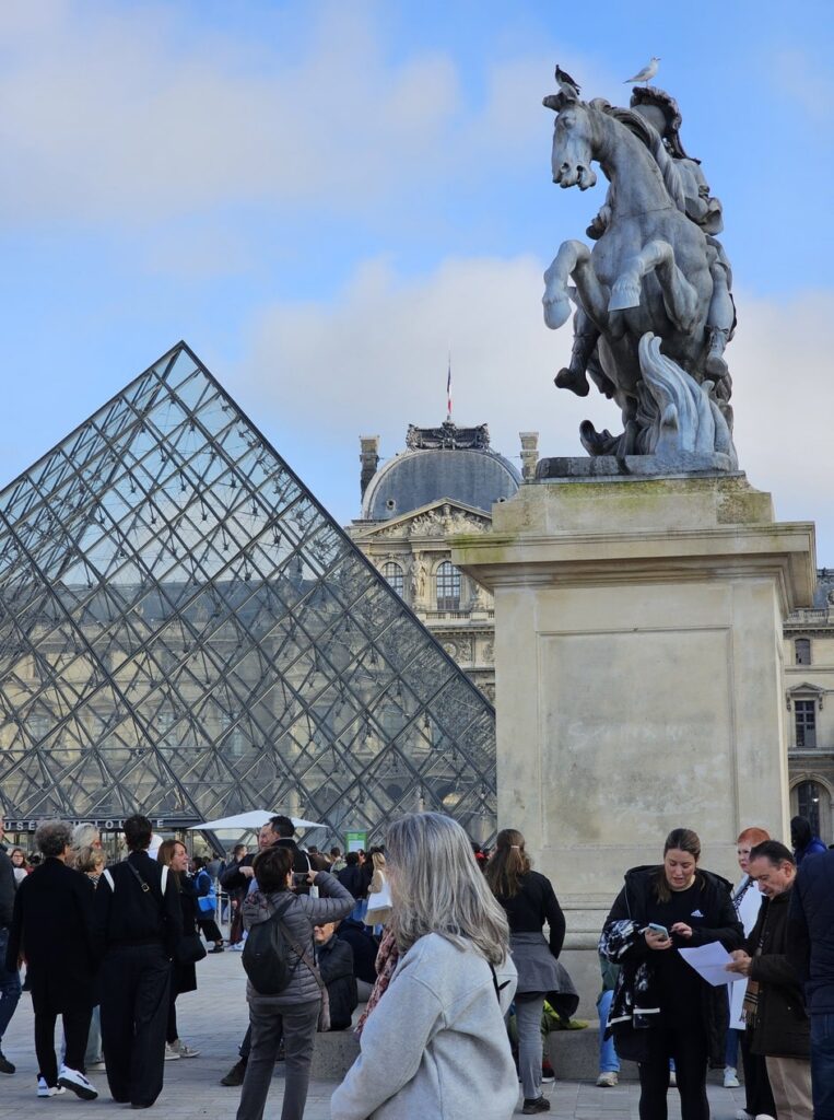 visiteurs qui marchent devant la pyramide du Musée du Louvre