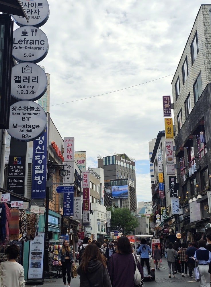 Rue Isandong à Séoul avec plusieurs commerces et enseignes coréennes colorées, illustrant la vie urbaine locale.
