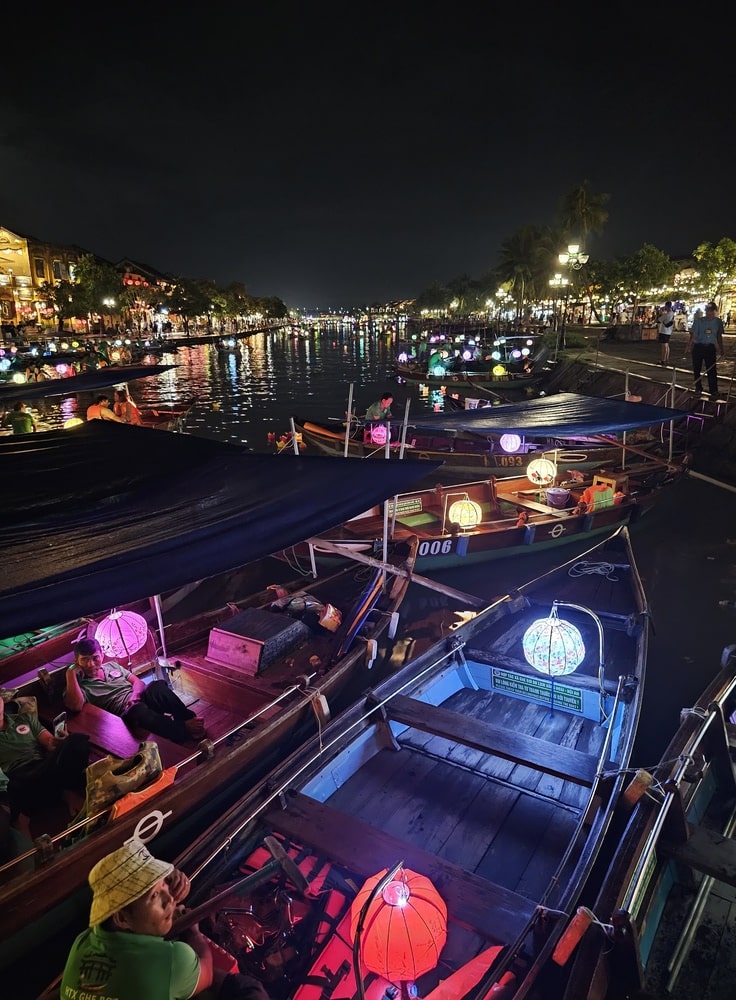 Les barques illuminées passent sous le pont de la rivière à Hoi An le soir pour déposer des offrandes sur l'eau, à voir en voyage au Vietnam