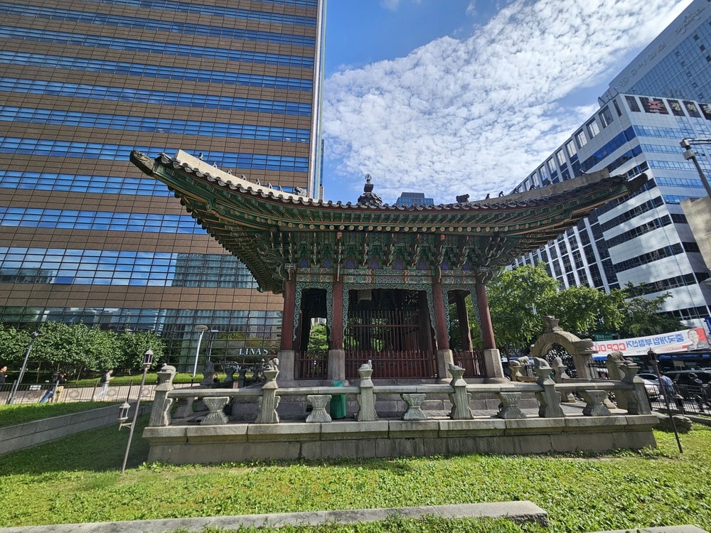 Temple traditionnel coréen avec son toit courbé et ses détails colorés, devant un bâtiment moderne à Séoul, illustrant le contraste entre patrimoine et modernité