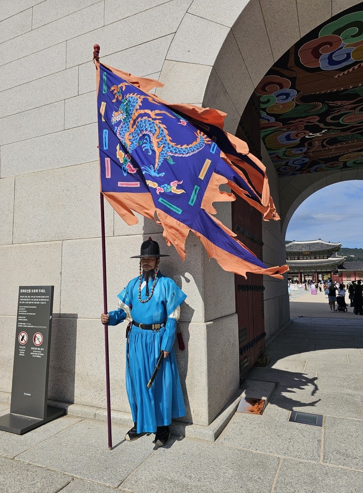Garde en tenue traditionnelle coréenne devant le palais de Gyeongbokgung, tenant un drapeau
