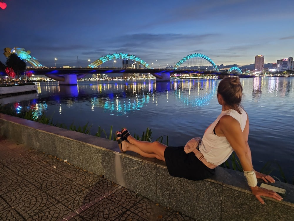 Ma soeur assise devant le pont-dragon, tout illuminé en bleu, pendant notre visite rapide de la ville, en voyage au Vietnam