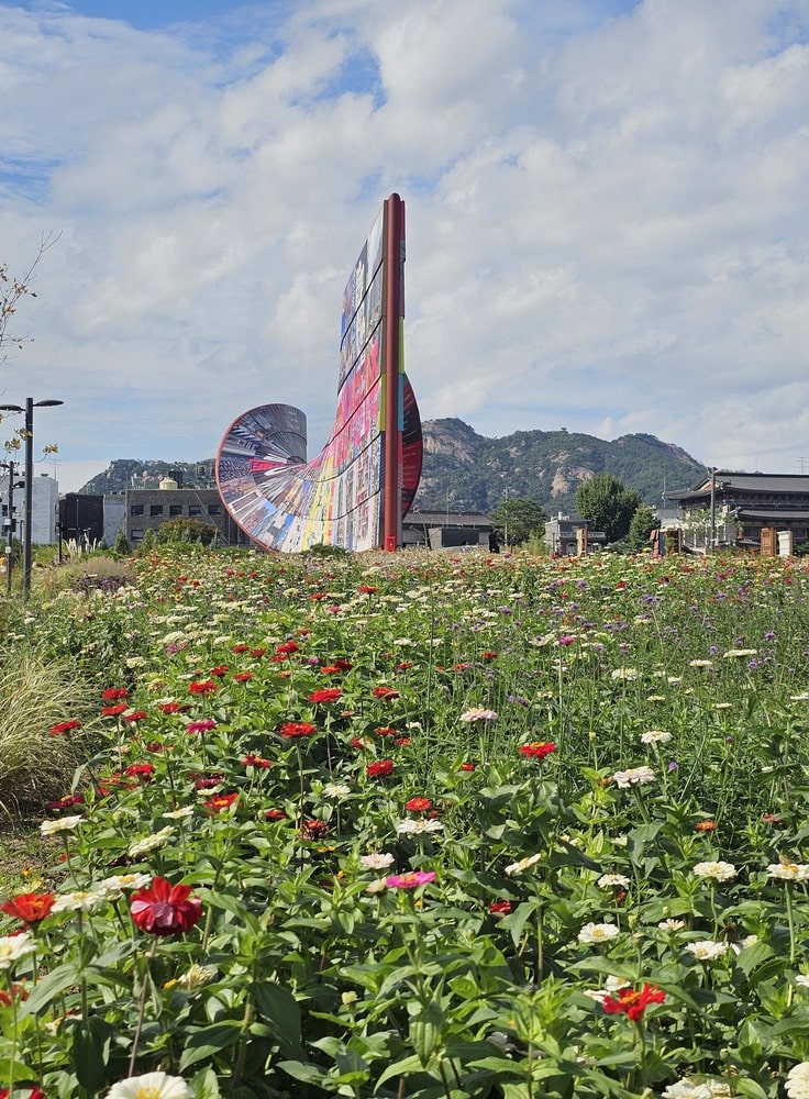 Mur artisanal avec citations et messages d’espoir au loin, entouré d’un jardin fleuri dans le parc de Songhyeon à Séoul.