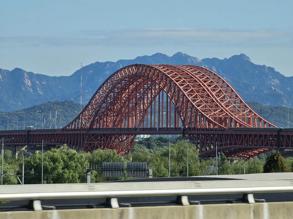 Pont métallique rouge vu depuis un autobus en route vers Séoul, avec les montagnes en arrière-plan